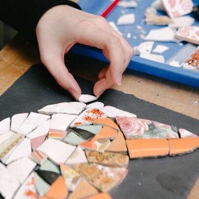 Hands making a mosaic picture of a ginger cat face. 