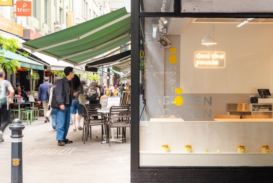 Soufflé pancake shop in a busy city laneway with people walking by.