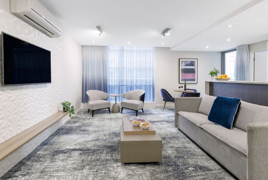 Hotel room lounge area with sofa, TV and seating.