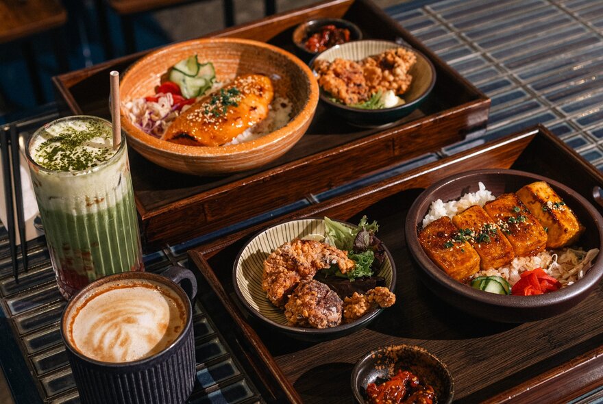 An array of Japanese food in bowls served on trays, with drinks. 