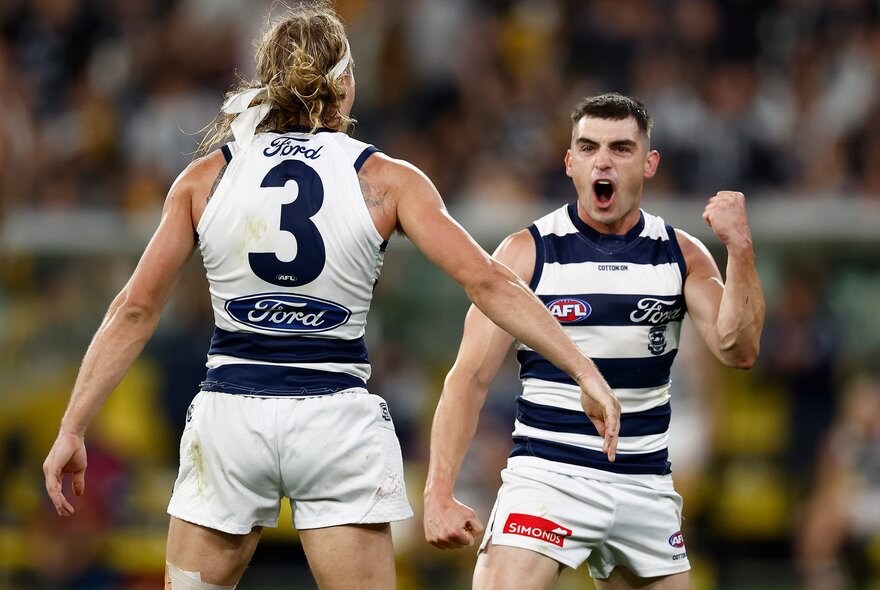 Two Geelong AFL players celebrating on the field.