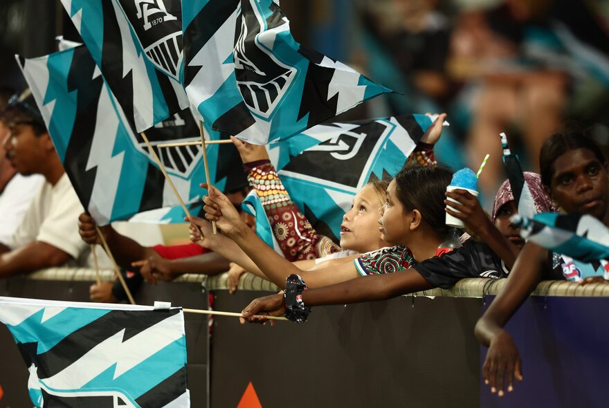 Port Adelaide AFL fans in the stadium holding up their team flags and banners during a game.