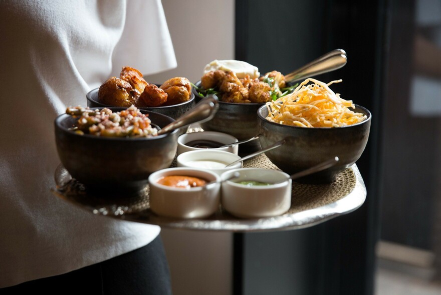 Person holding a tray of small bowls of food and sauces.