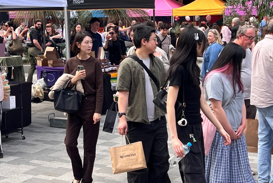 People browsing vendor stalls and walking through an outdoor urban market.