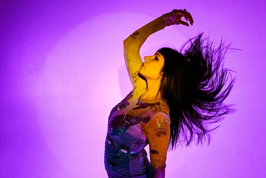 Person dancing against a purple light, their hair blowing behind them.