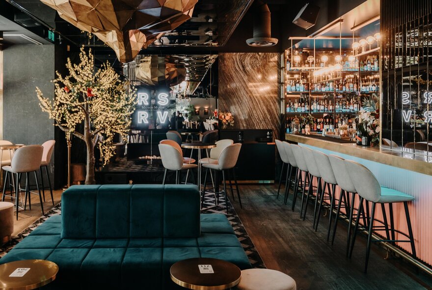 Interior of a bar and restaurant, with high stools at the bar area, a wall of drinks, and tables and chairs arranged on the floor.