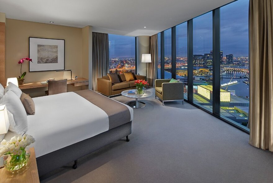 Hotel room looking out onto the Yarra River and city views through corner feature windows, with grey carpet and drapes.