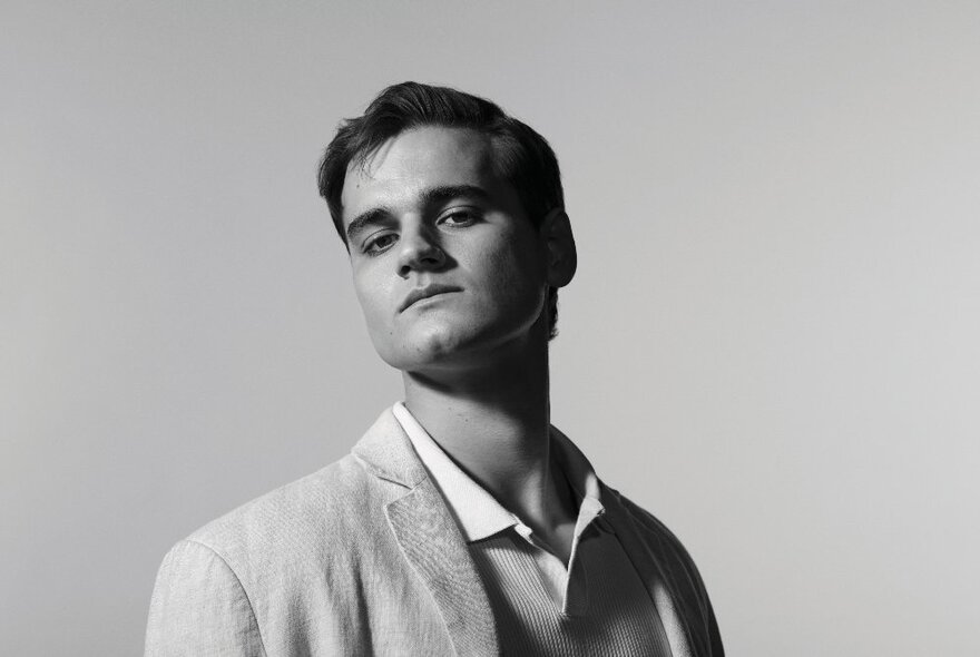 Actor posing as an arrogant young man wearing a linen suit, his head on the side.