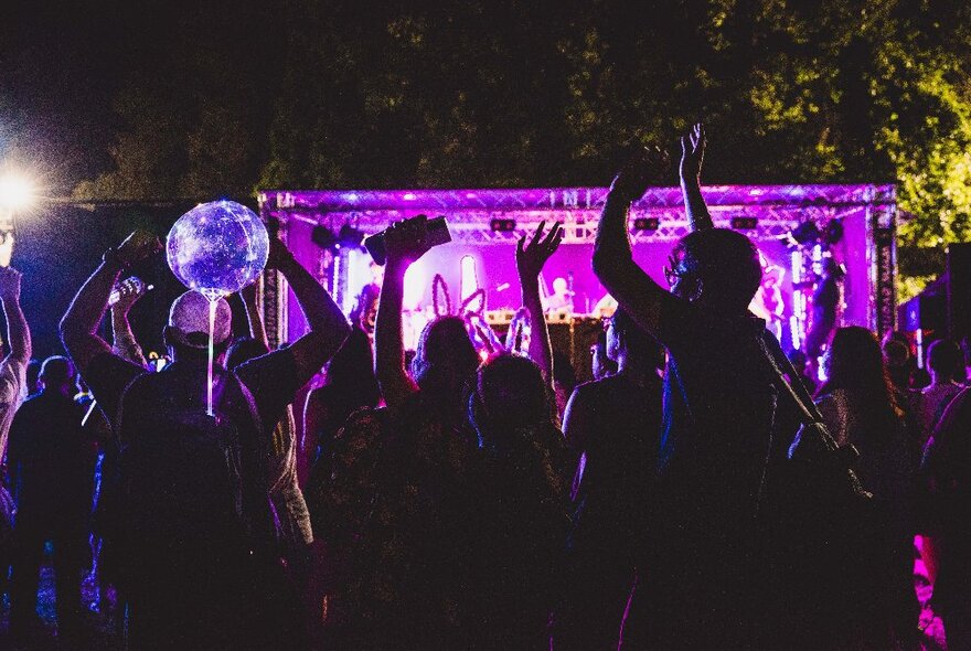 Revellers dancing at a party outdoors with purple lights. 