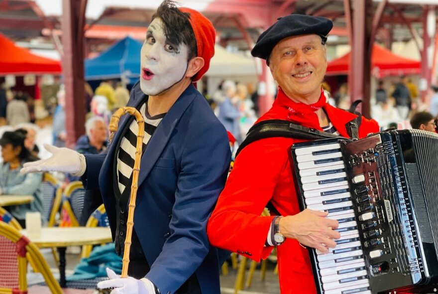 Two roving performers at the French Bastille Day celebrations at Queen Victoria Market, one playing a piano accordion, the other performing mime in costume.