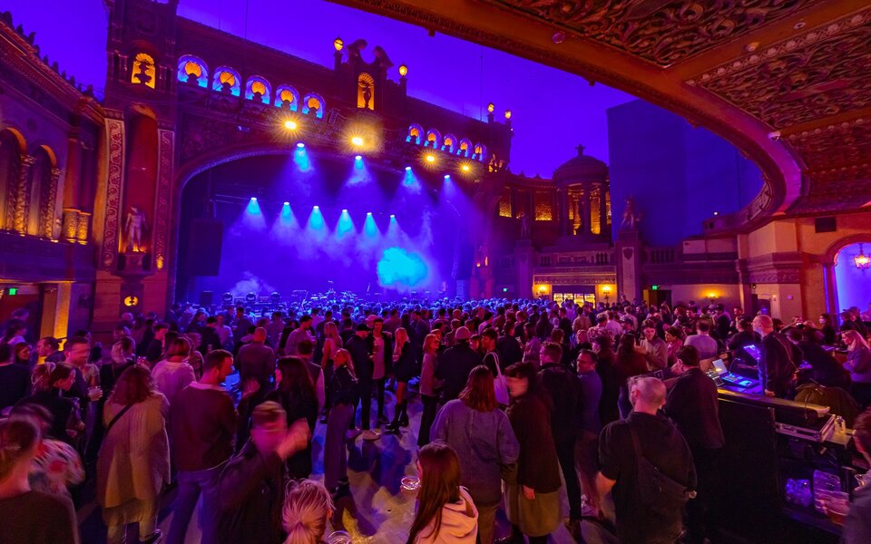 A stage with a grand facade to look like a building, with crowds waiting for a band to come onstage.