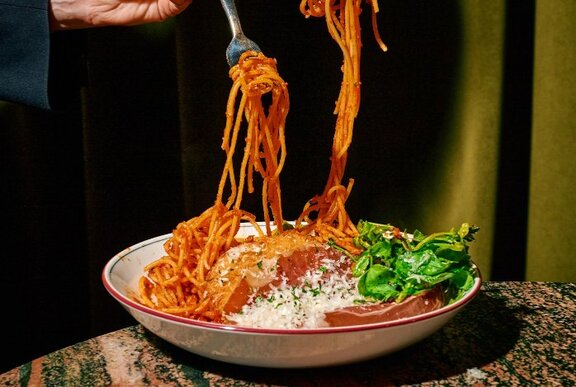 Spaghetti being forked from a dish with meat and salad.