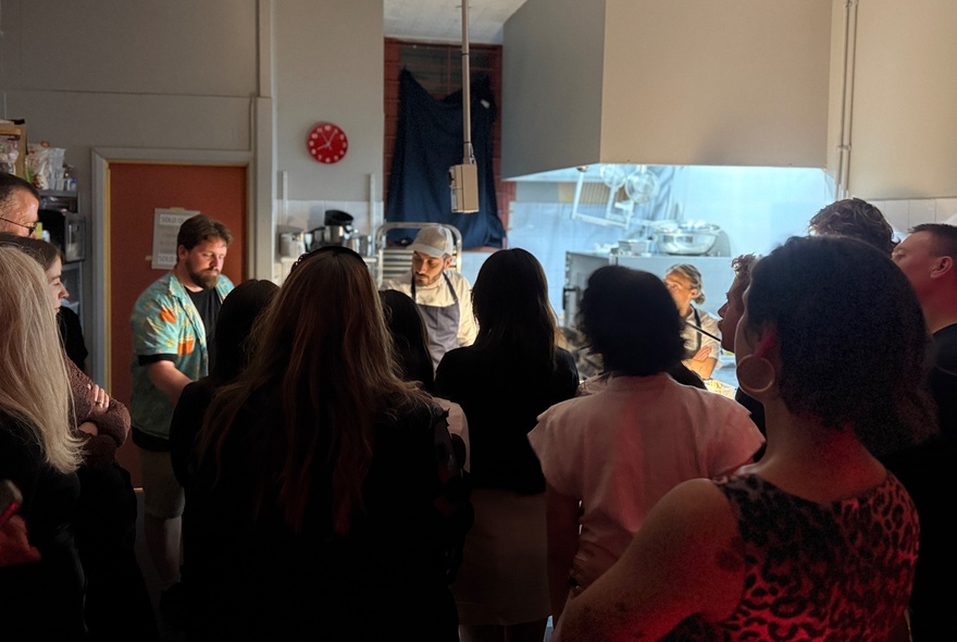 A small group of people watching a chef prepare a meal in a dim room. 