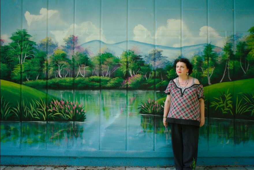 A woman in front of a large mural featuring a lake and mountains in the distance. 