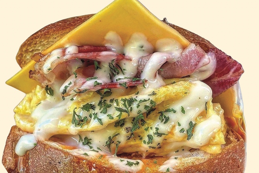 Close-up detail of an egg sandwich, with melted cheese, scrambled egg and bacon.