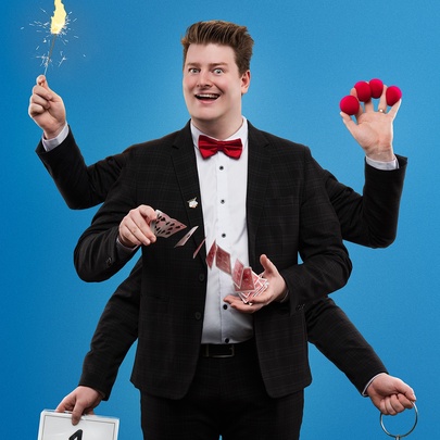 Liam ‘LJ’ Jumpertz in a tuxedo with two sets of extra arms performing multiple magic tricks simultaneously. 