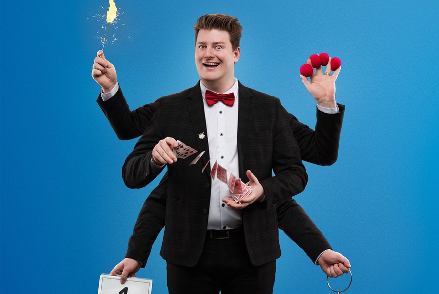 Liam ‘LJ’ Jumpertz in a tuxedo with two sets of extra arms performing multiple magic tricks simultaneously. 