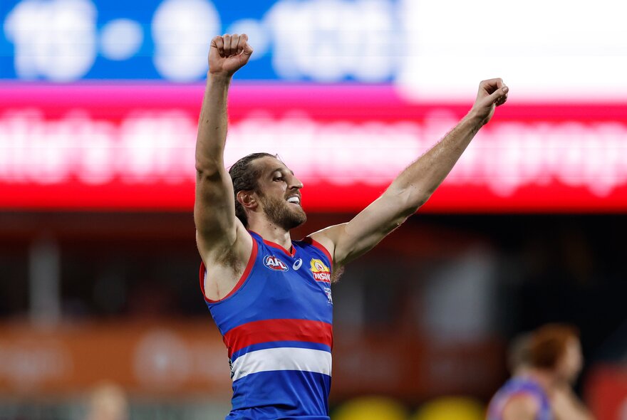 Marcus Bontempelli from the Western Bulldogs cheering with pumped fists raised in the air, on the footy field.