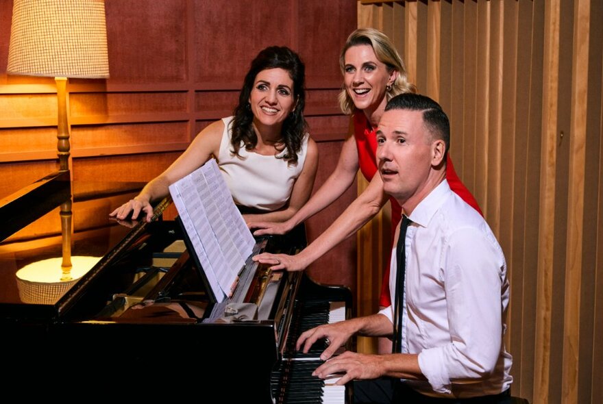 Members of the group Simply Brill - a man on piano and two women standing singing and smiling. 