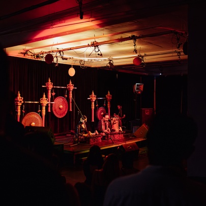 An indoor stage with traditional Indonesian gamelan instruments, including large gongs and metallophones, illuminated by dramatic red lighting.