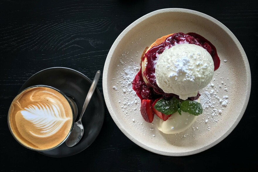 Cup of coffee next to a plate of pancakes and ice cream.