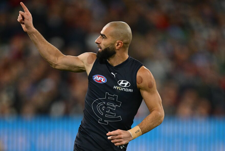 Carlton AFL football player with arms outstretched during a match.
