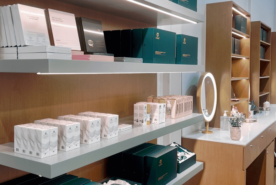 Shelves with rows of beauty products with a mirror and table.