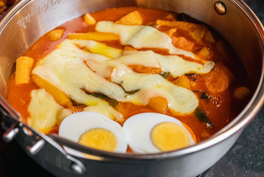 A metal bowl filled with rice cakes, special sauce and egg.