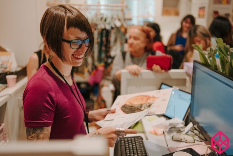 Smiling woman at a shop counter processing a sale on a computer.