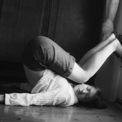 Woman lying on her back, her legs bent over her head, feet against a window.