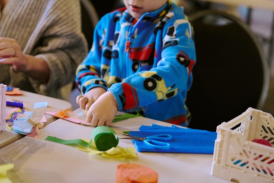 A small child busy at a crafting table in a fleecy top with trucks on it. 