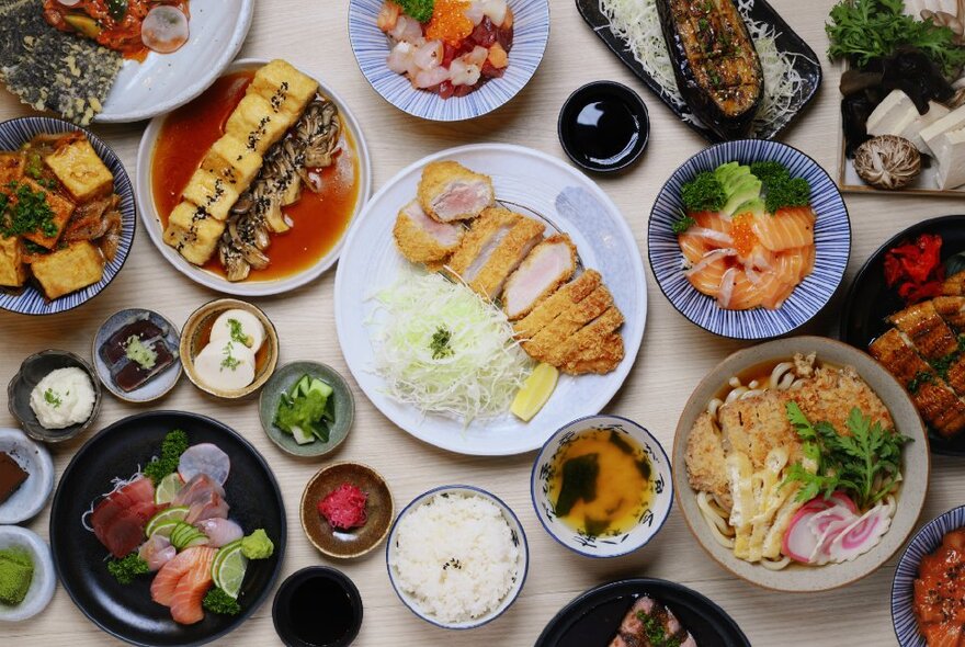 Overhead view of a table loaded with Japanese dishes of food including rice, chicken and condiments.