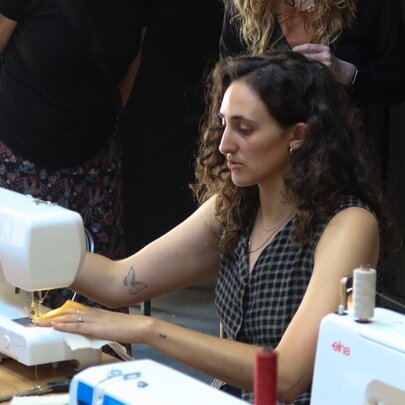 Woman seated at a workstation working at a sewing machine.