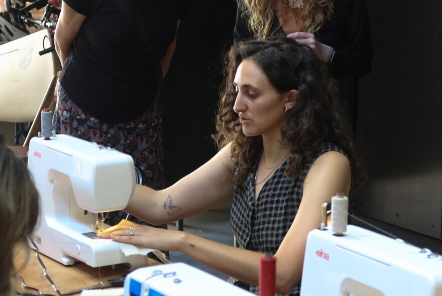 Woman seated at a workstation working at a sewing machine.