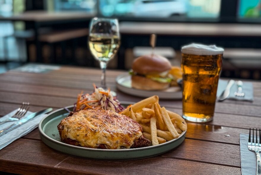 Two dishes of food on a wooden table, with a pot of beer and a glass of wine.