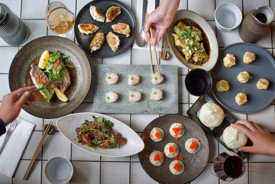 Hands selecting from an assortment of dumplings, buns and salads.