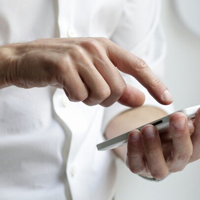 Hands holding a mobile phone, with a finger poised to press.