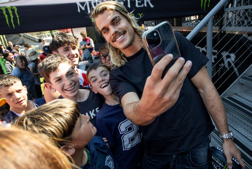 AFL footballer Bailey Smith taking a selfie with lots of children around him.