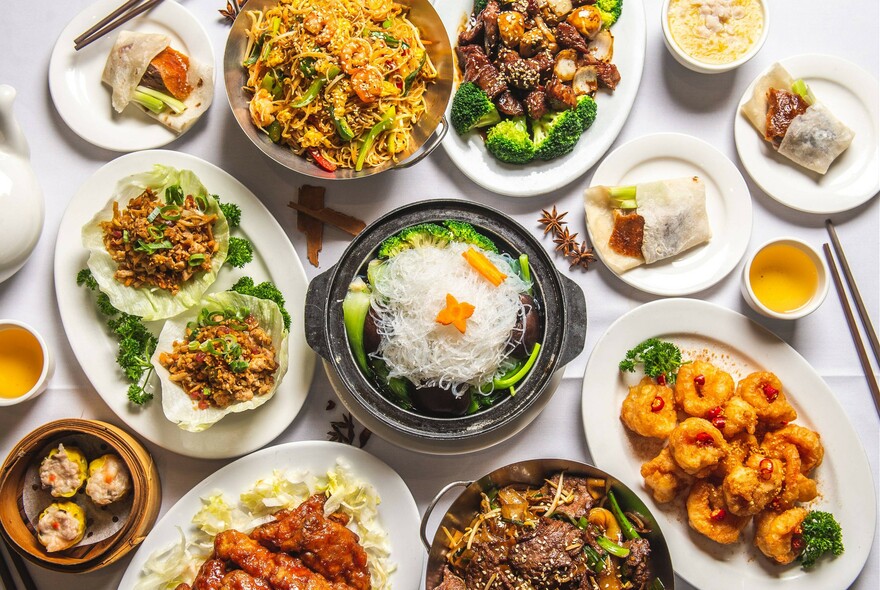 Array of dishes on white tablecloth, including rice and stir-fries.