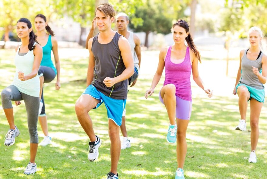 A group of people in workout clothing doing a fitness class in a leafy park setting.