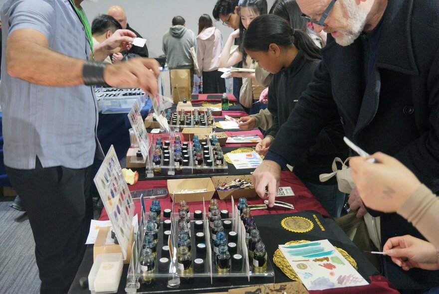 Customers looking at pen and stationery supplies for sale at an exhibition stall.