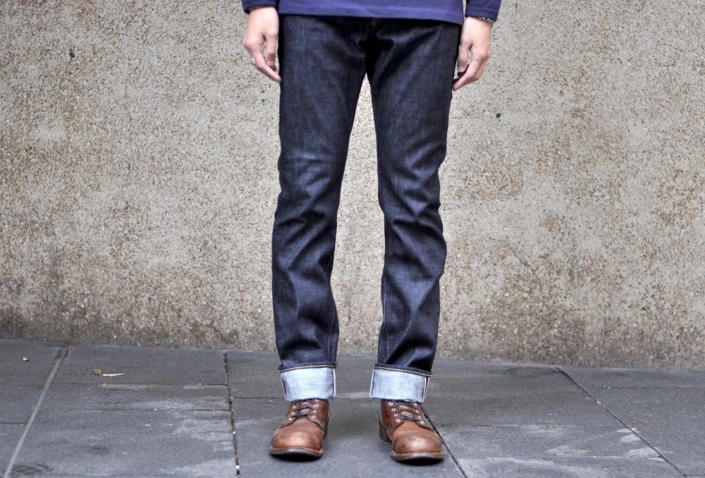 Man wearing brown boots and dark blue jeans with the bottoms rolled up.