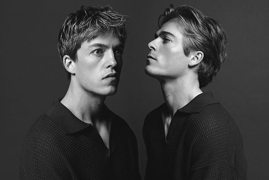 Two young men in dramatic lighting with heads on an angle, both wearing black.
