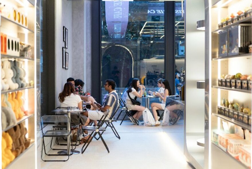 Sleek  interior of retail cafe space with people seated at tables, large windows, and display areas showing collectible toys and objects.