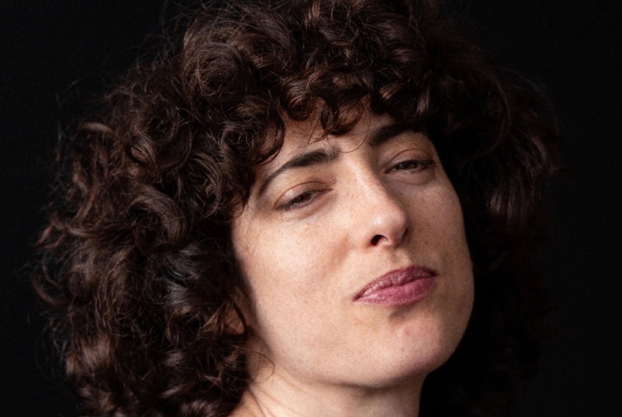 Portrait of comedian, Hannah Camilleri, with curly brown hair and a slight smile.