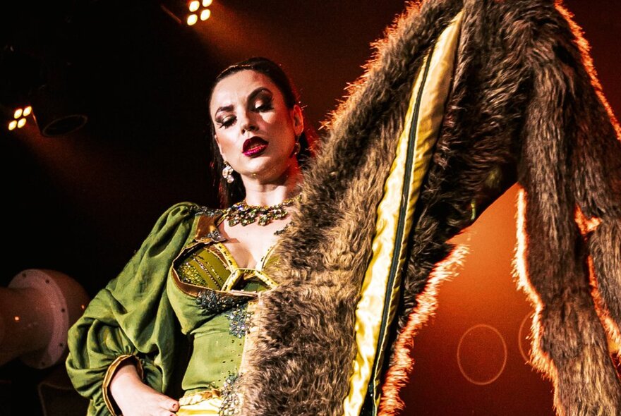 A burlesque dancer performing in a green dress, holding up a fur stole. 