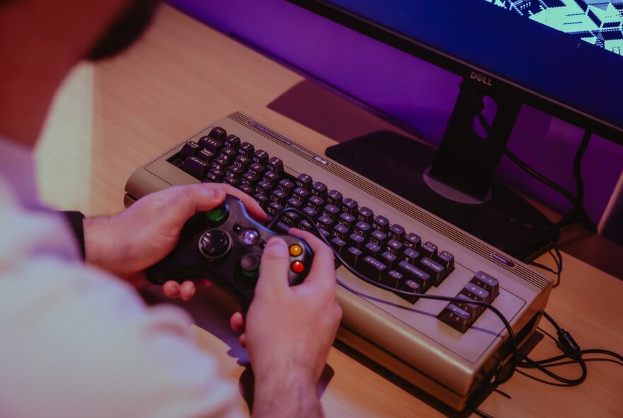 Hands holding a game console in front of a keyboard.