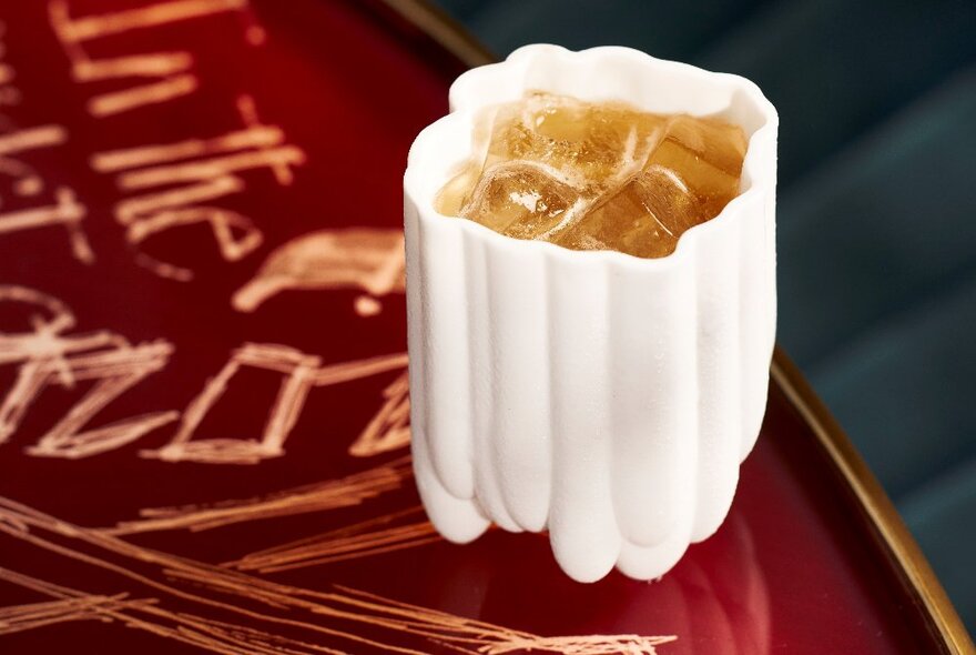 A table with etched patterns and letters holding a drink in a white cup.