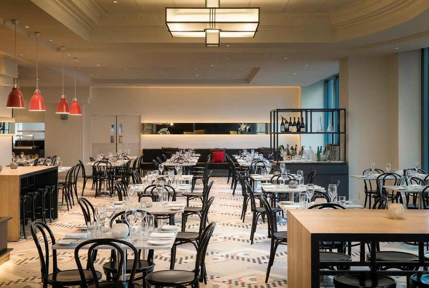 Hotel dining room with row of tables, chairs and benches.