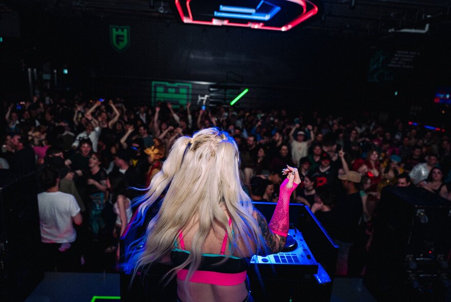 DJ with long grey hair viewed from behind at a mixing desk in a dark venue.